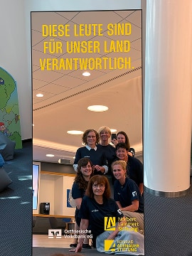 Kampagnenspiegel in einem Innenraum, davor sieben Personen